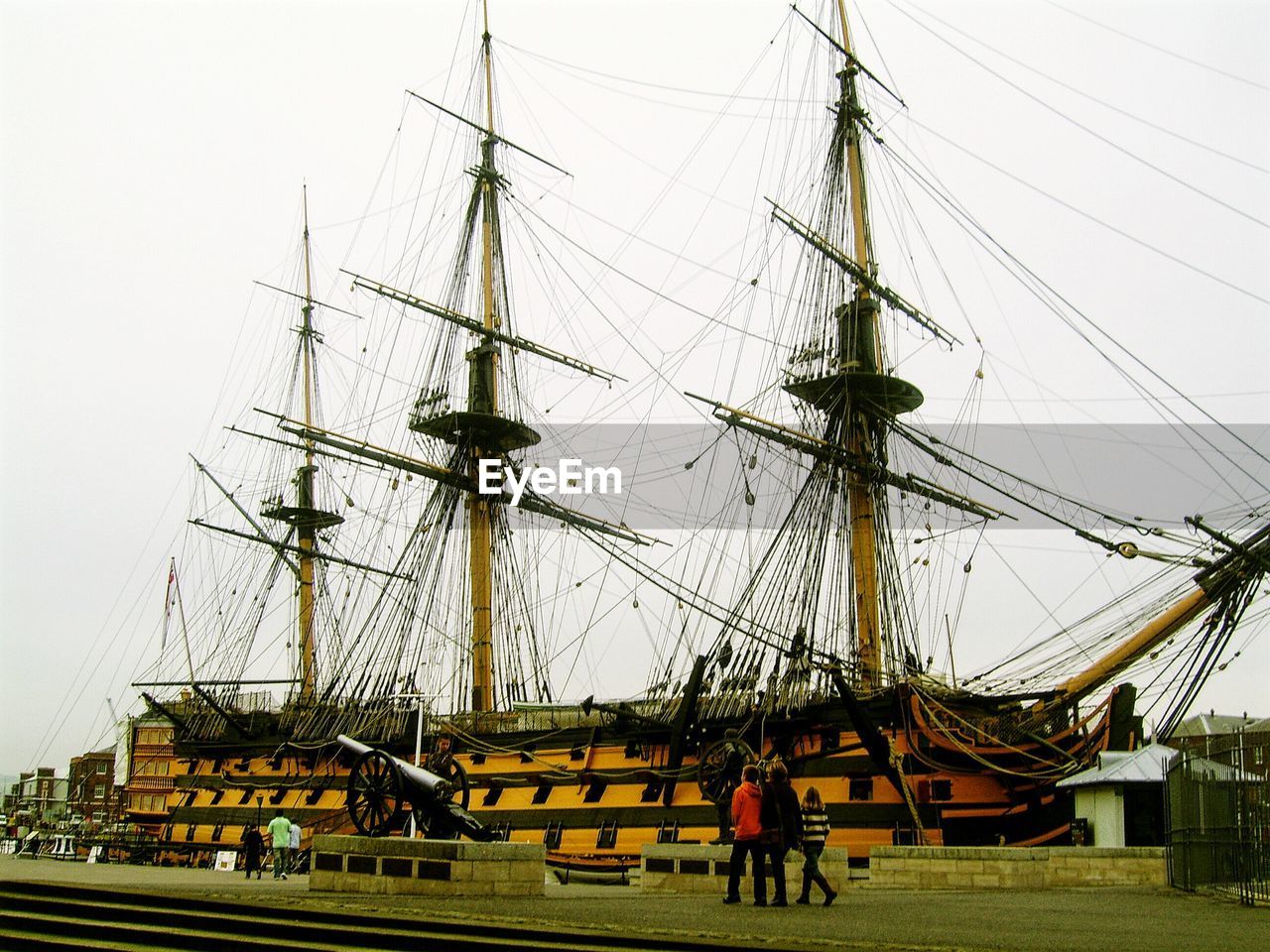 People visiting historic ship moored at harbor against clear sky
