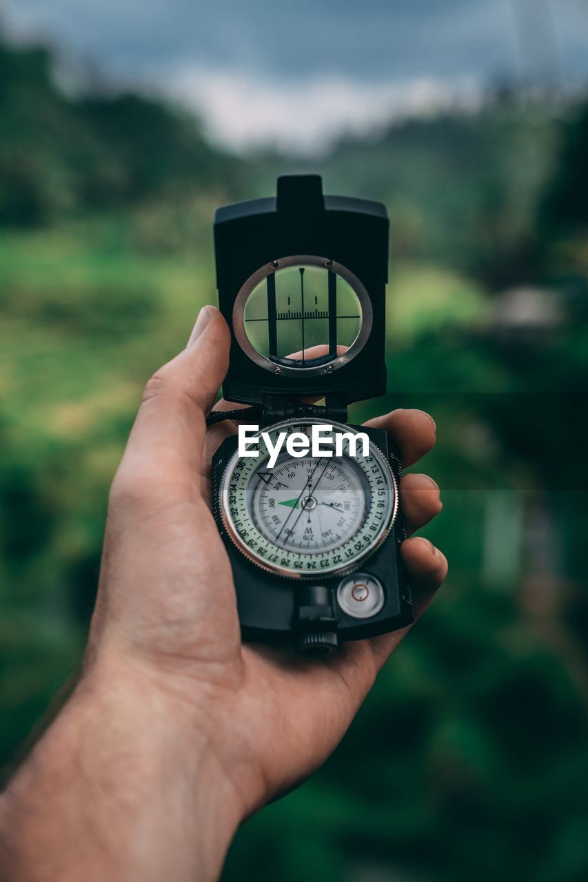 Cropped hand holding navigational compass against plants