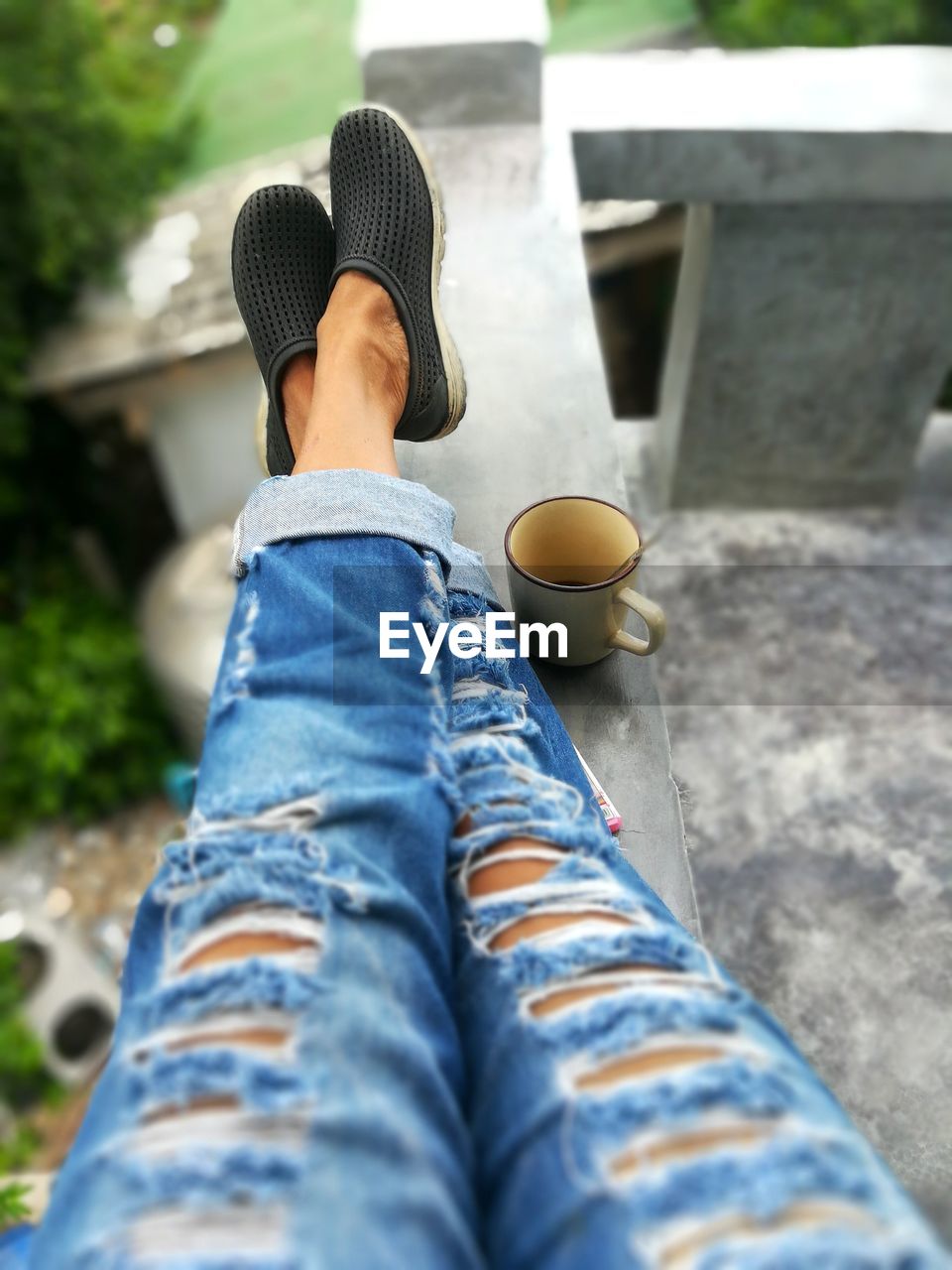 Low section of woman sitting by coffee cup on railing