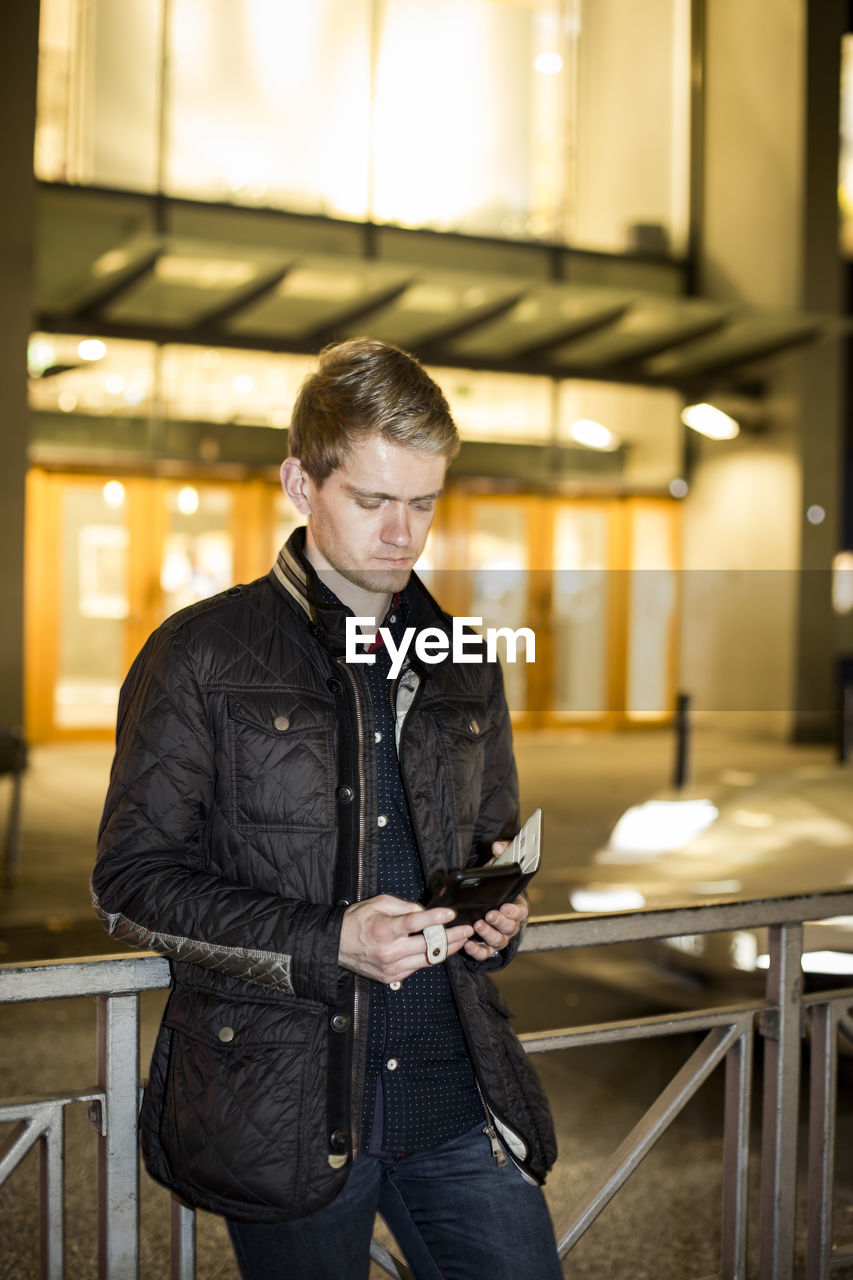 Young man using mobile phone while standing by railing