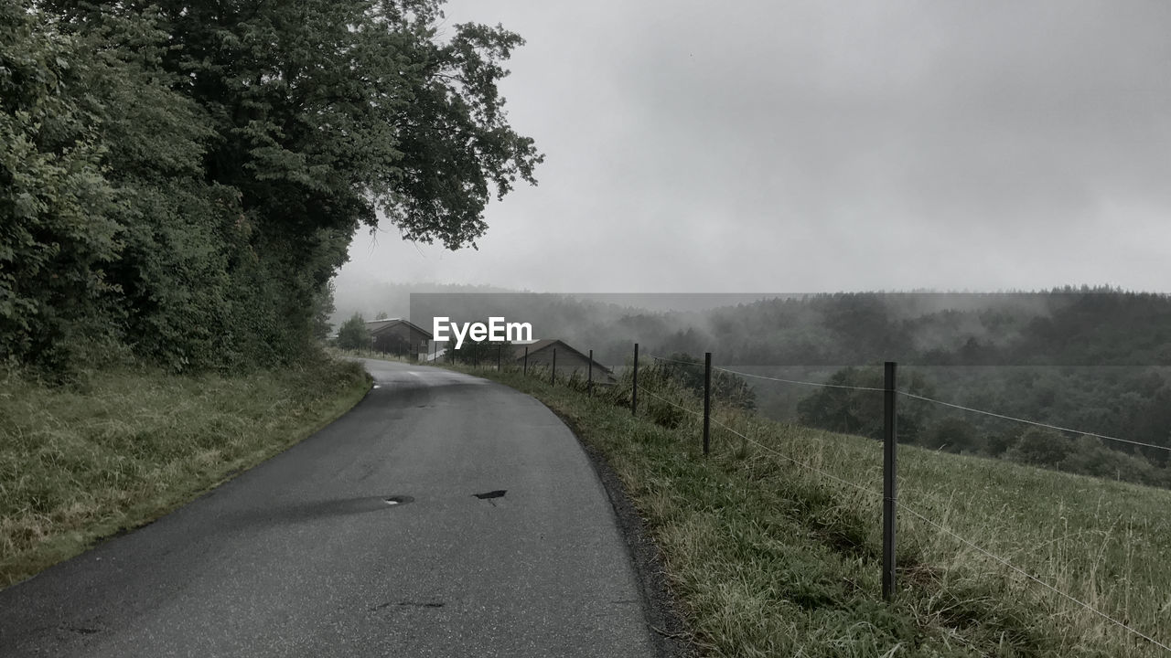 ROAD AMIDST TREES AND LANDSCAPE AGAINST SKY