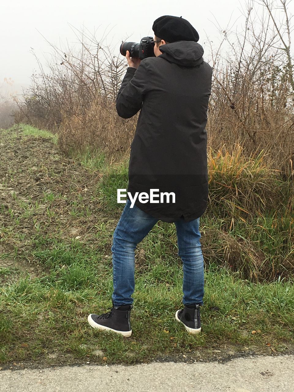 Rear view of man photographing with camera while standing on field