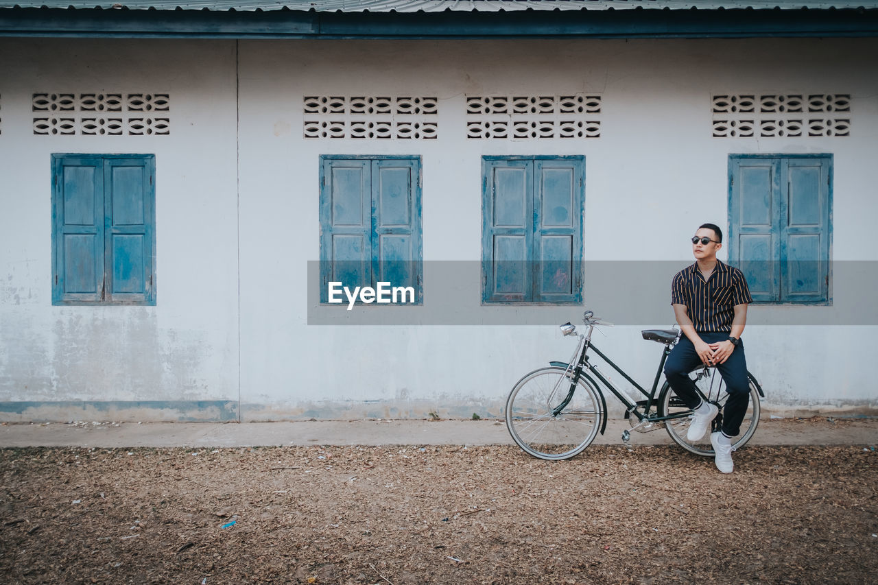 Full length of man sitting outside house on bicycle