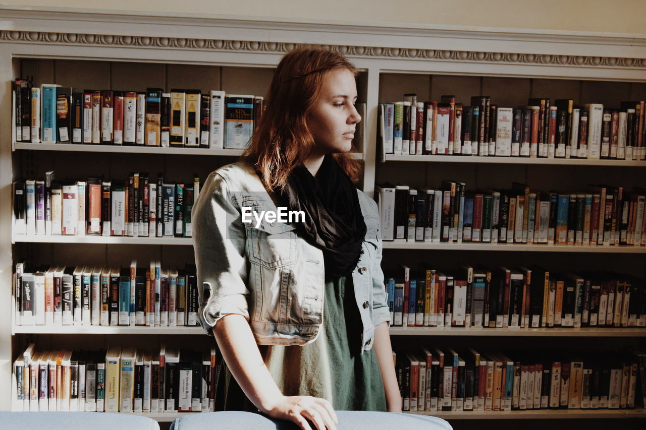 Young woman standing against bookshelf in library