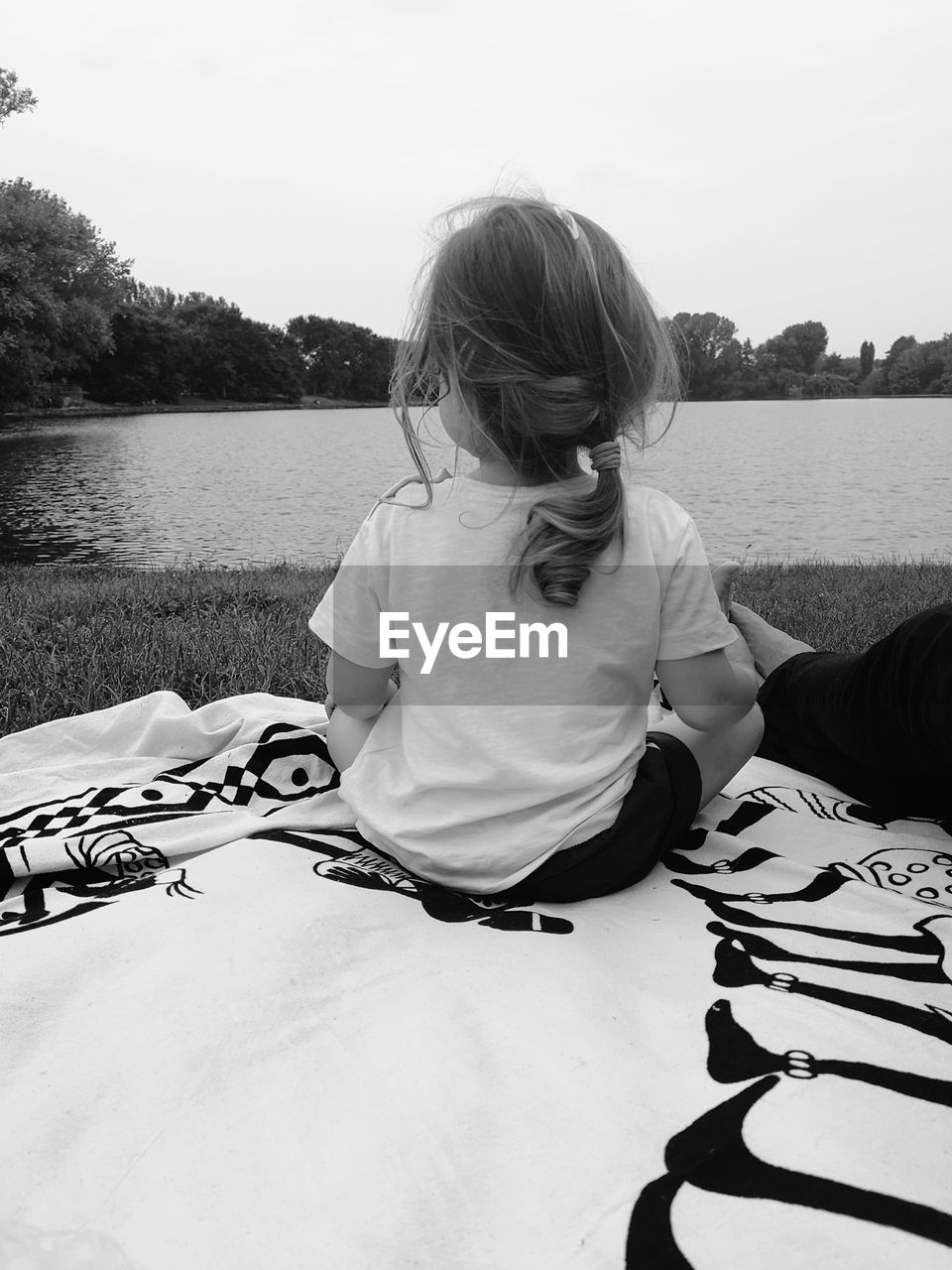 Rear view of little girl relaxing by lake against sky