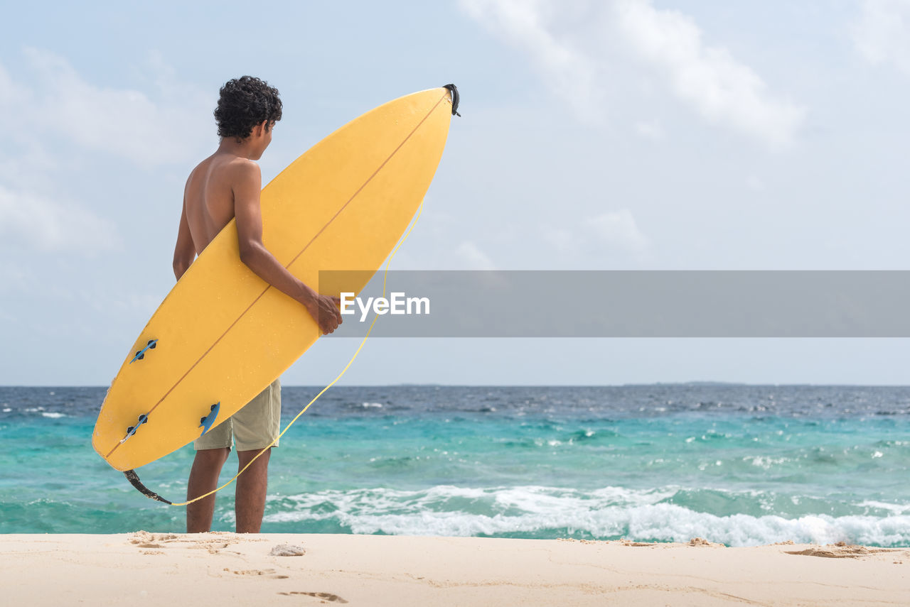 Male surfer standing on shore against sea at beach