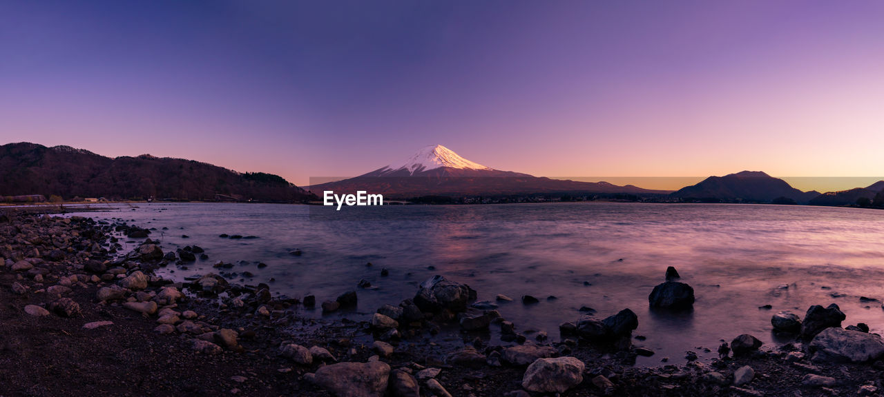 SCENIC VIEW OF LAKE BY MOUNTAINS AGAINST SKY DURING SUNSET