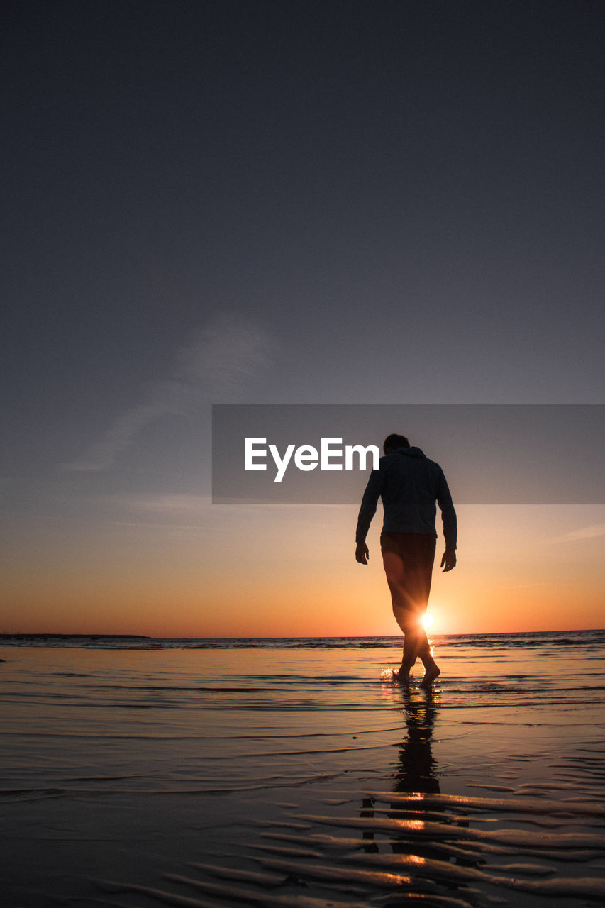 Silhouette man wading in sea during sunset