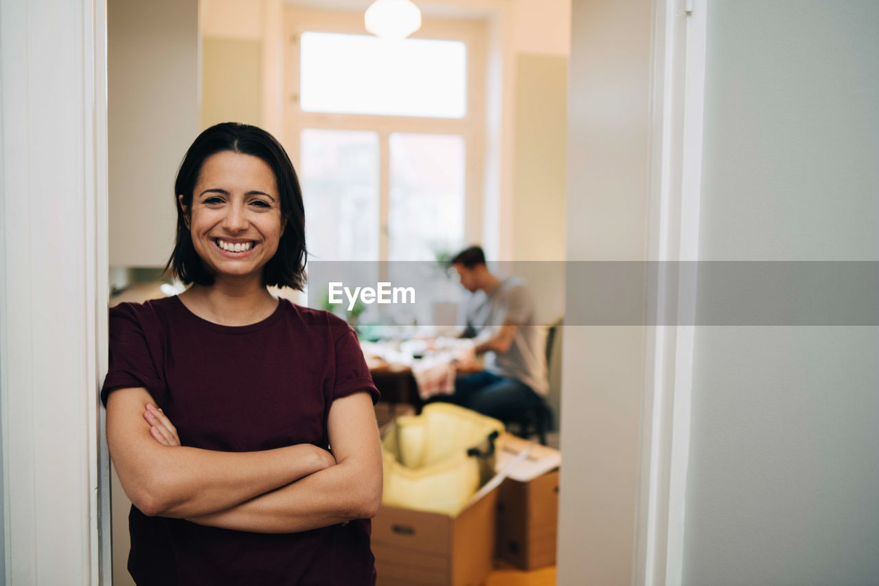 Portrait of smiling woman with arms crossed leaning on doorway at new home