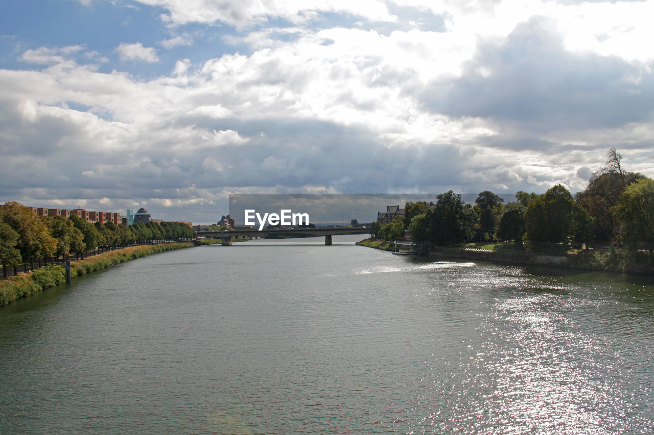 Scenic view of calm river in city against cloudy sky