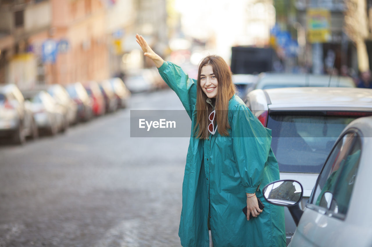 Portrait of smiling woman gesturing while standing by cars on street in city