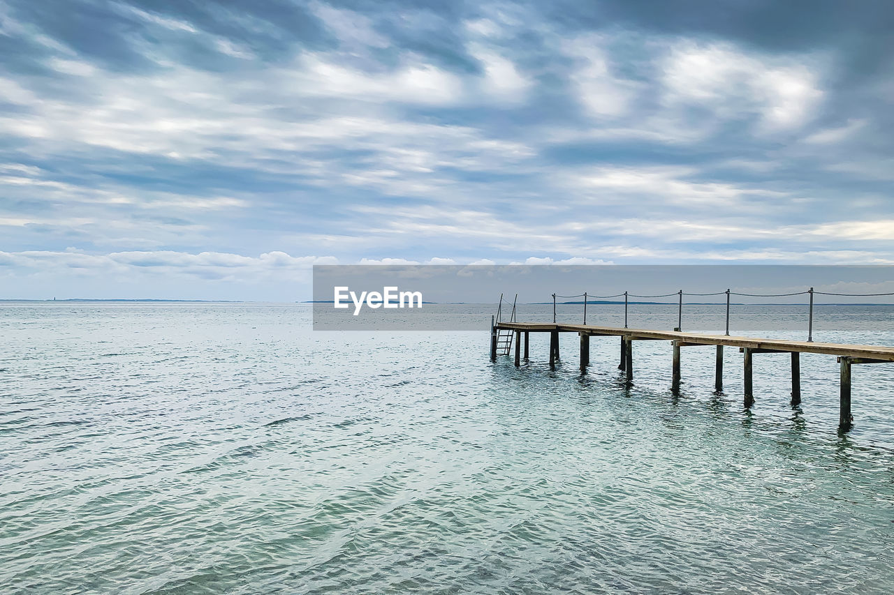 WOODEN POSTS ON PIER OVER SEA AGAINST SKY