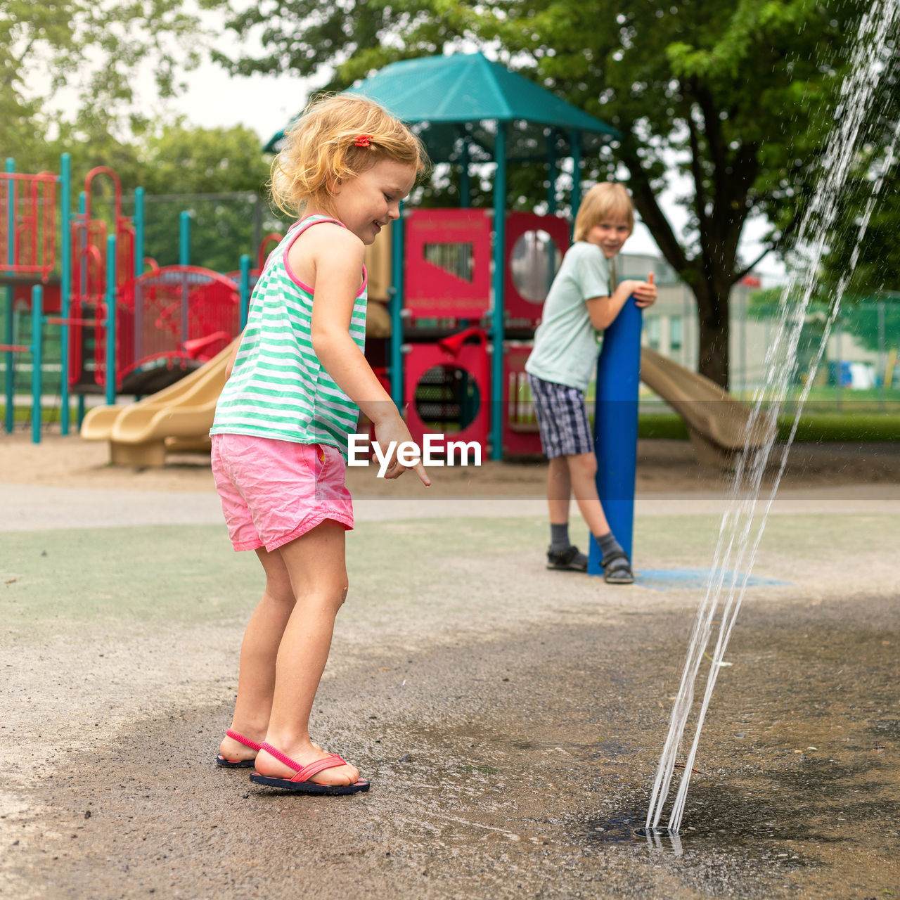 Little happy smiling children playing with water at splash pad in the local public park playground 