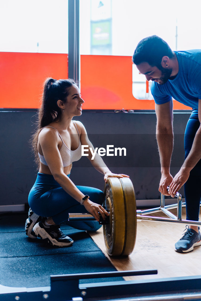 Side view portrait of young woman exercising in gym lifting 