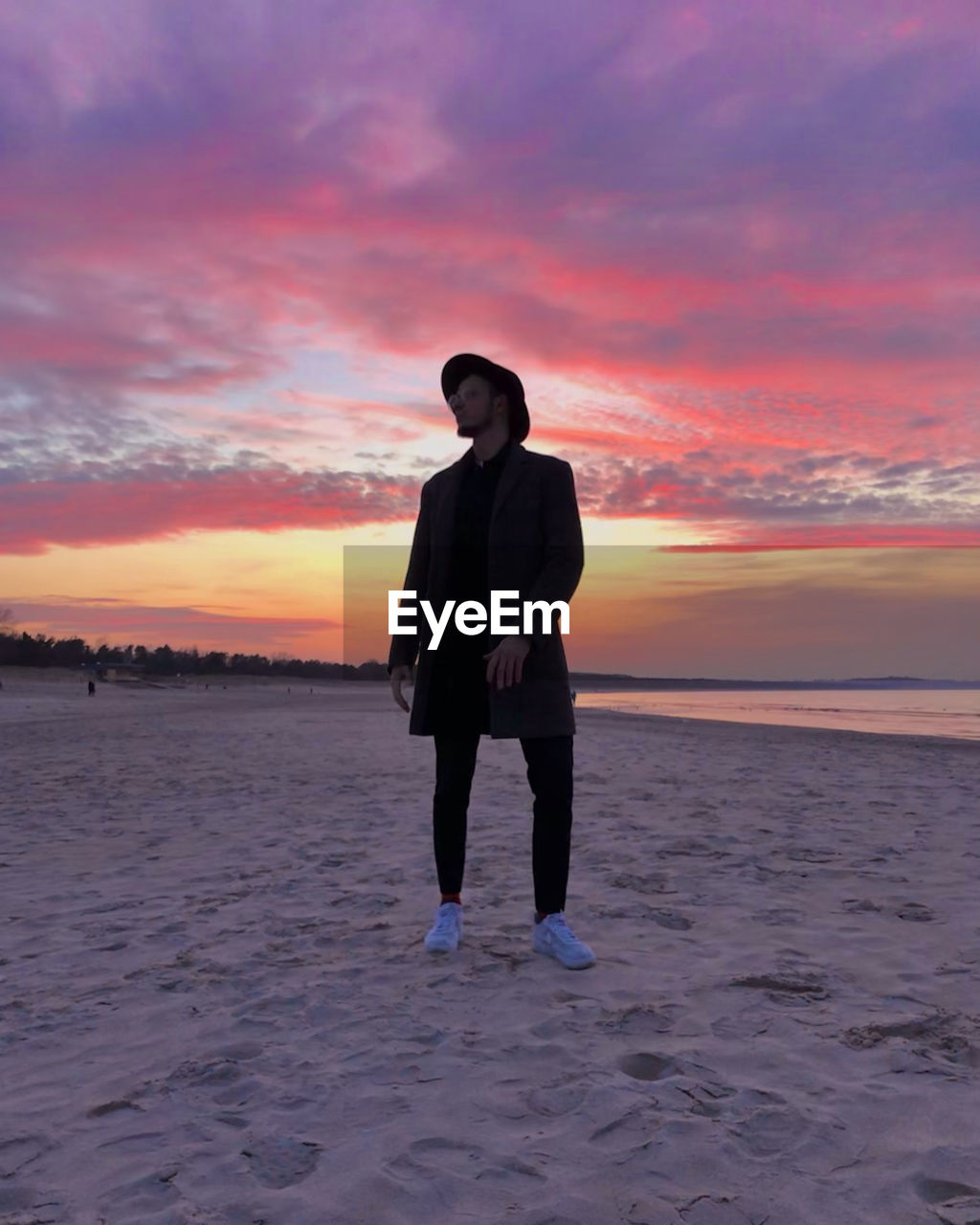 FULL LENGTH OF WOMAN STANDING ON BEACH DURING SUNSET