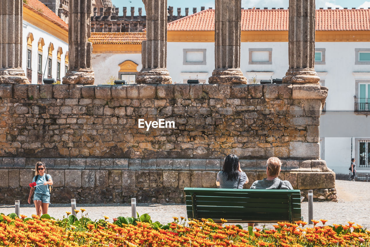 PEOPLE SITTING ON BENCH AGAINST BRICK WALL