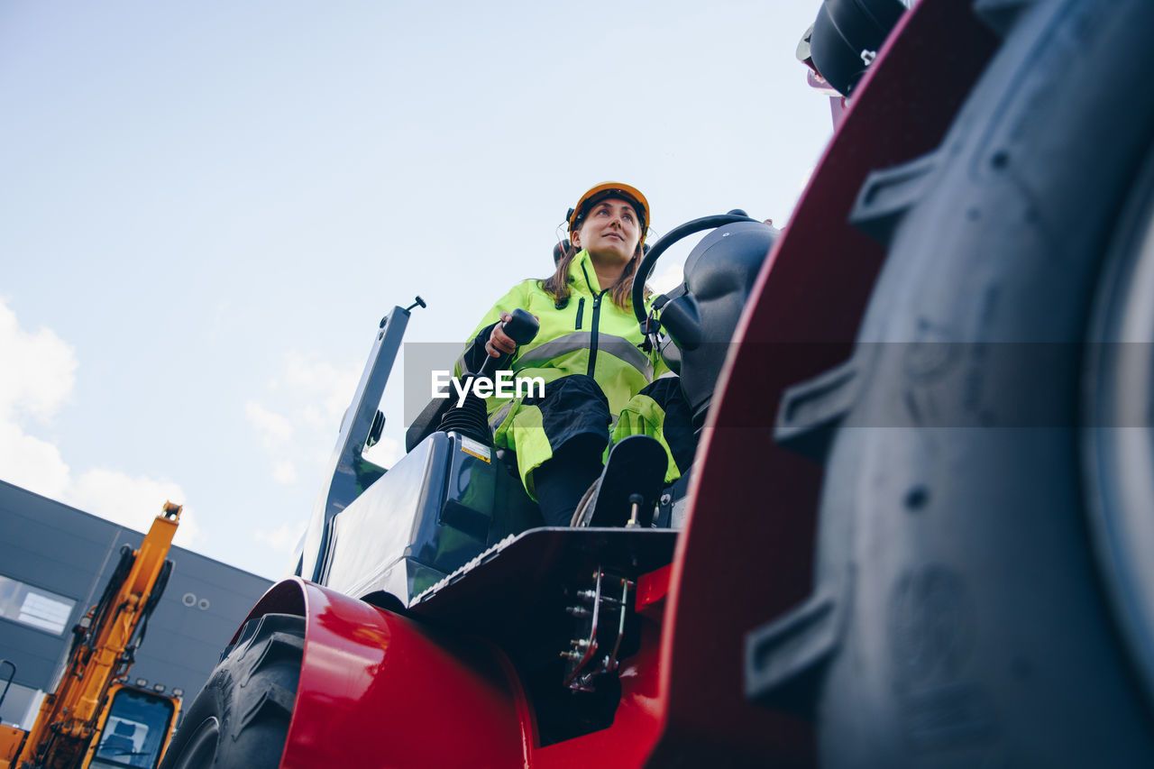 Woman driving construction vehicle against sky