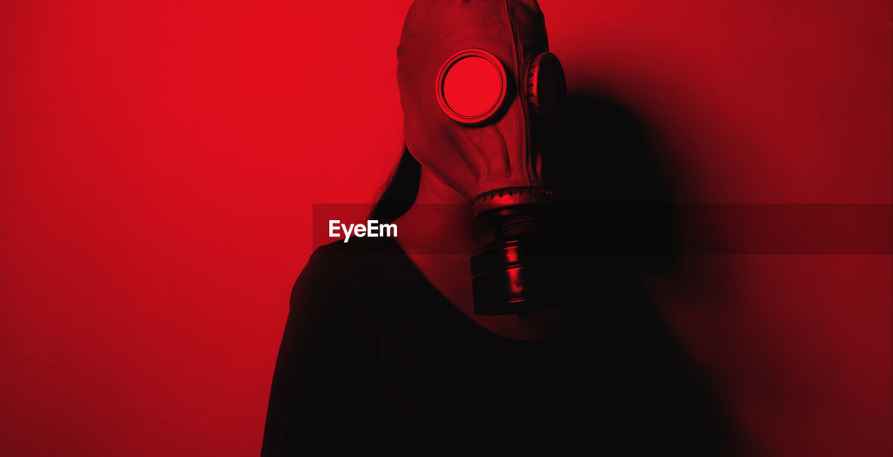Woman wearing gas mask standing against red wall