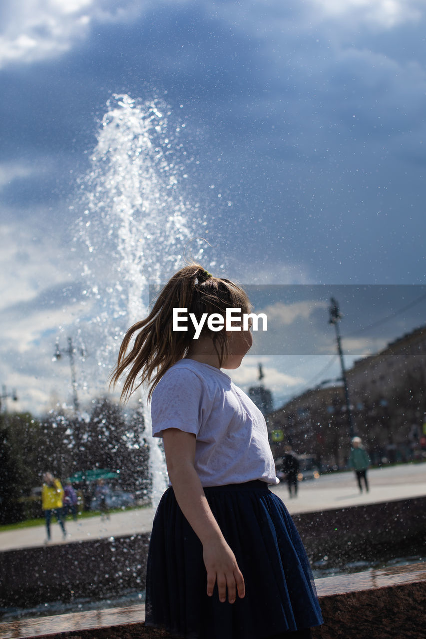 Happy little cute girl having fun in splashes a fountain