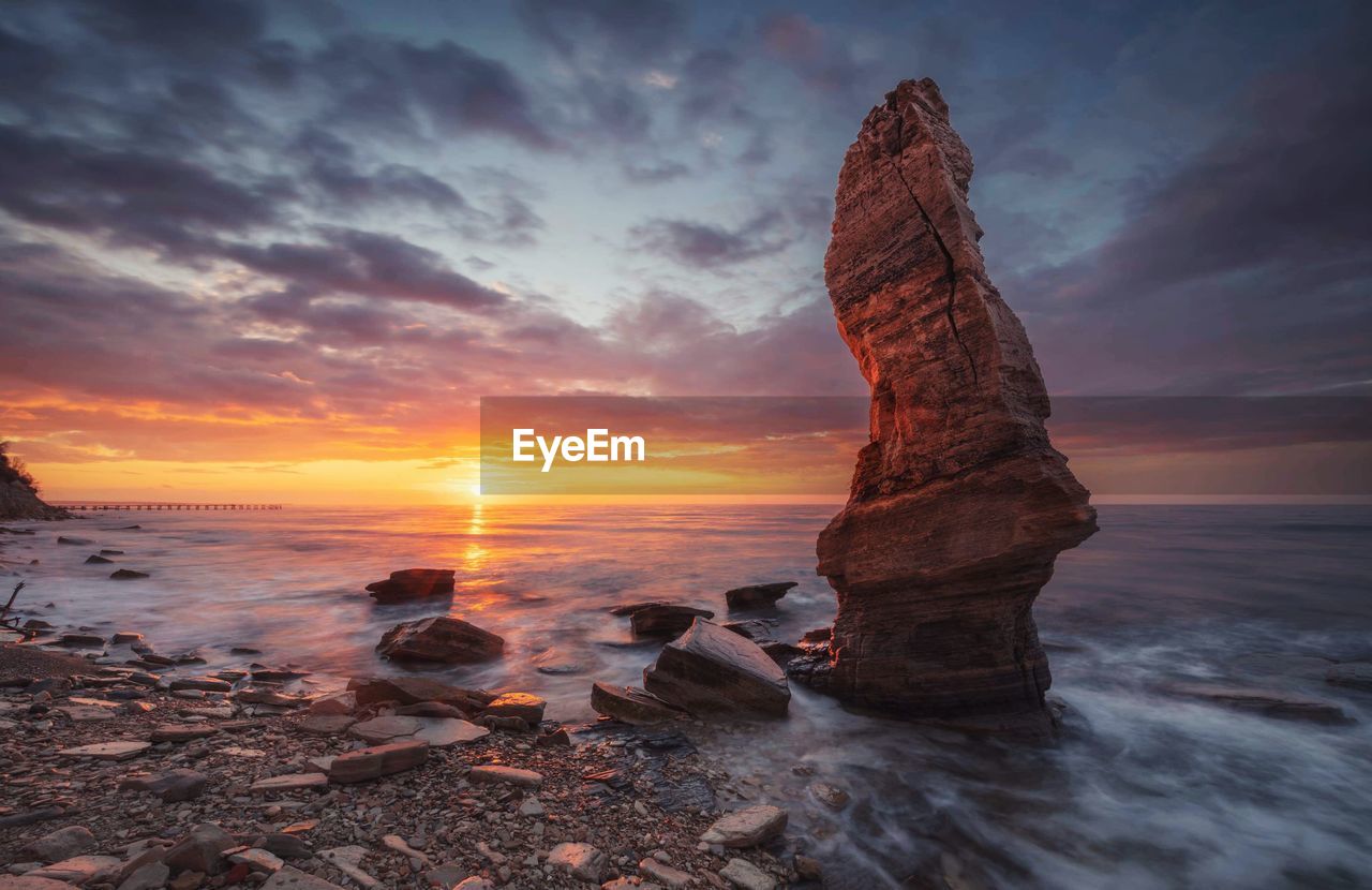 Rock formation on beach against sky during sunset