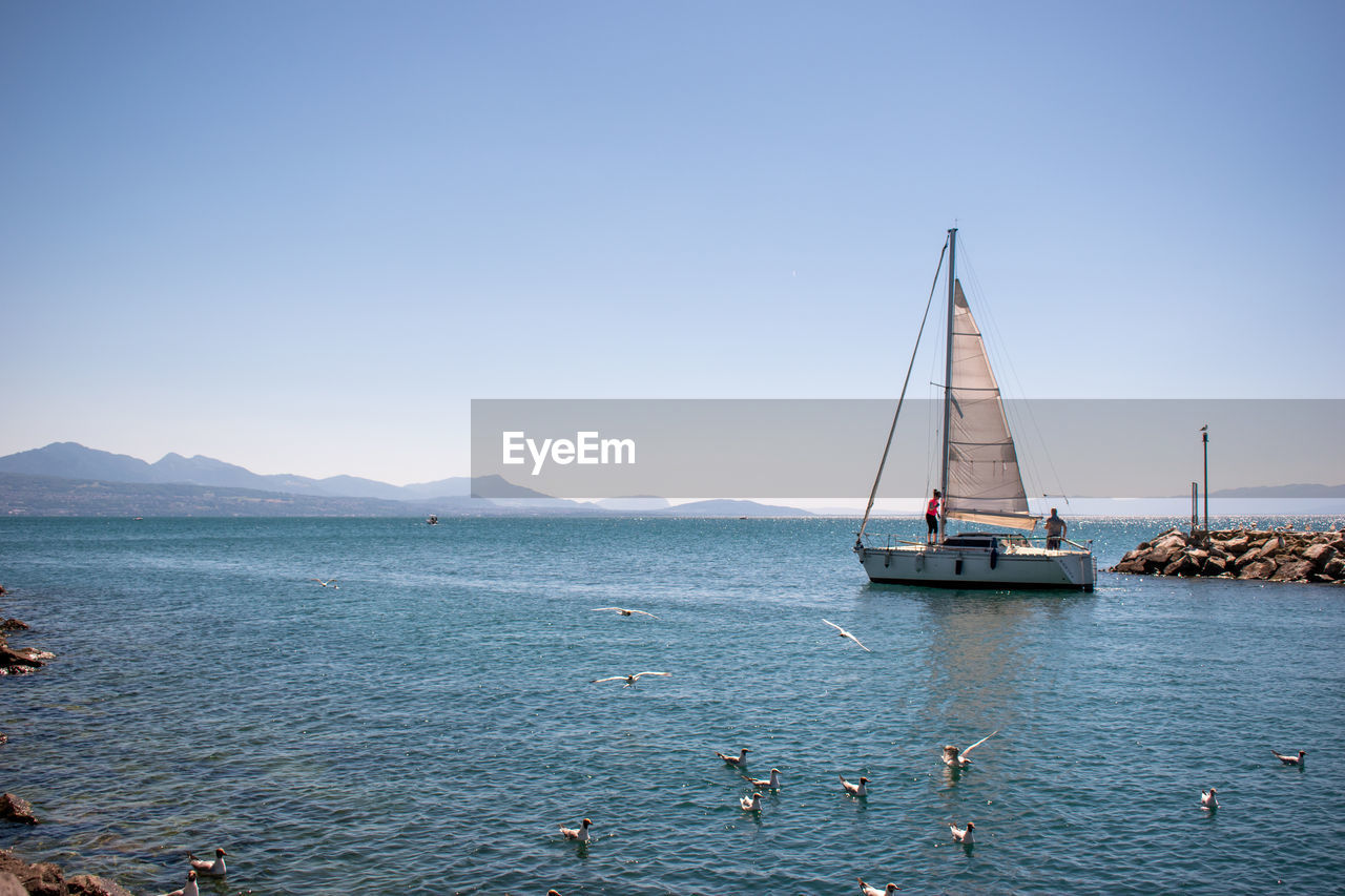 water, nautical vessel, sea, sailboat, transportation, sailing, mode of transportation, sky, travel, nature, bay, sailing ship, beauty in nature, boat, vehicle, blue, clear sky, ship, horizon, scenics - nature, travel destinations, yacht, ocean, environment, tranquility, vacation, tranquil scene, holiday, pole, mast, trip, luxury, idyllic, yachting, outdoors, coast, summer, day, no people, mountain, land, sports, beach, copy space, tourism, architecture, sunny, landscape, adventure, craft, shore, watercraft, bay of water, tall ship, sunlight, motion