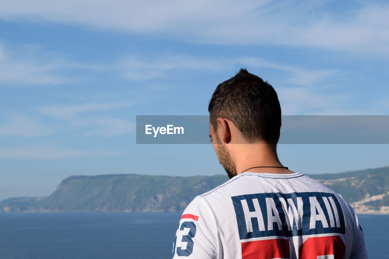 Rear view of man standing by sea against sky