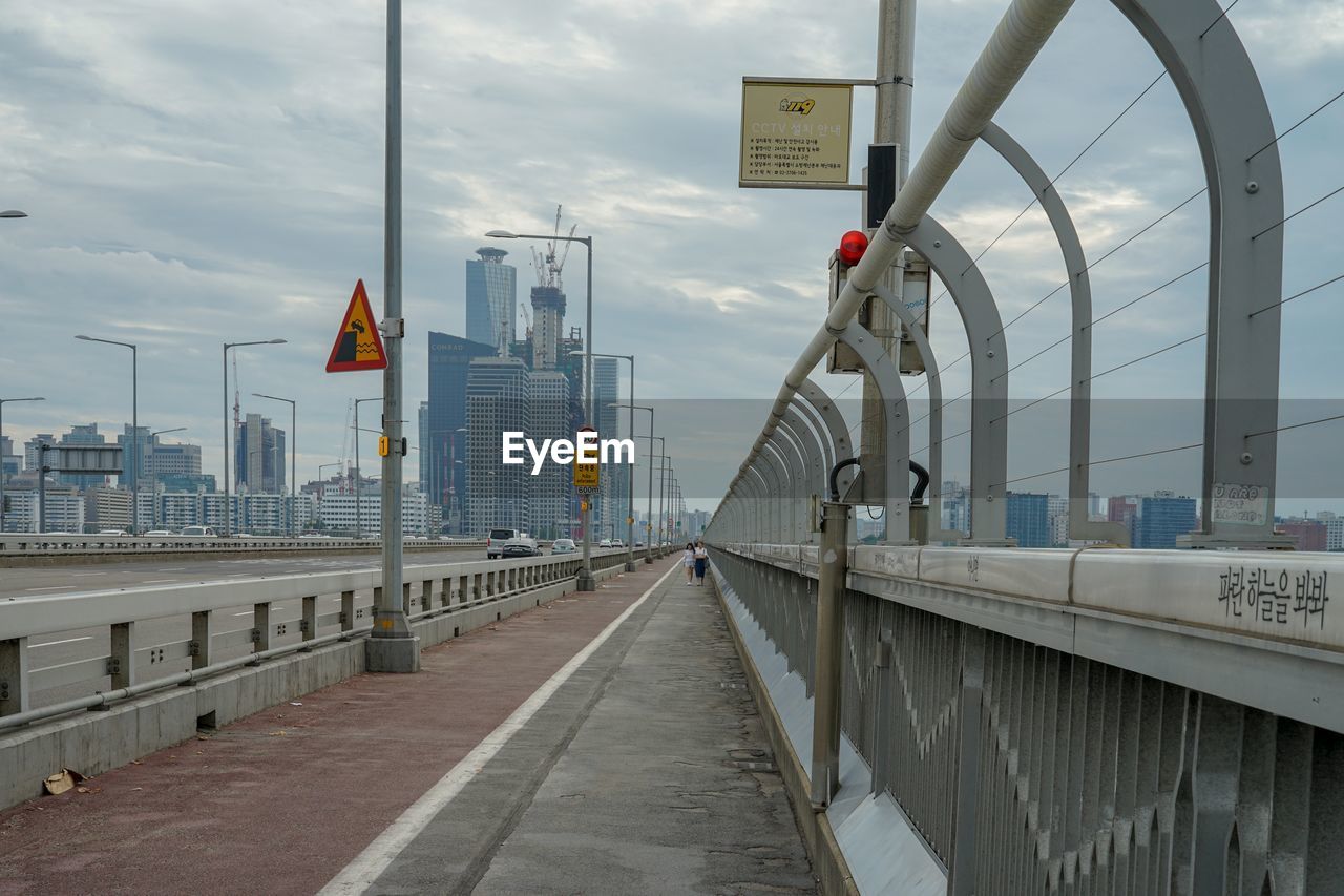 Bridge in city against cloudy sky