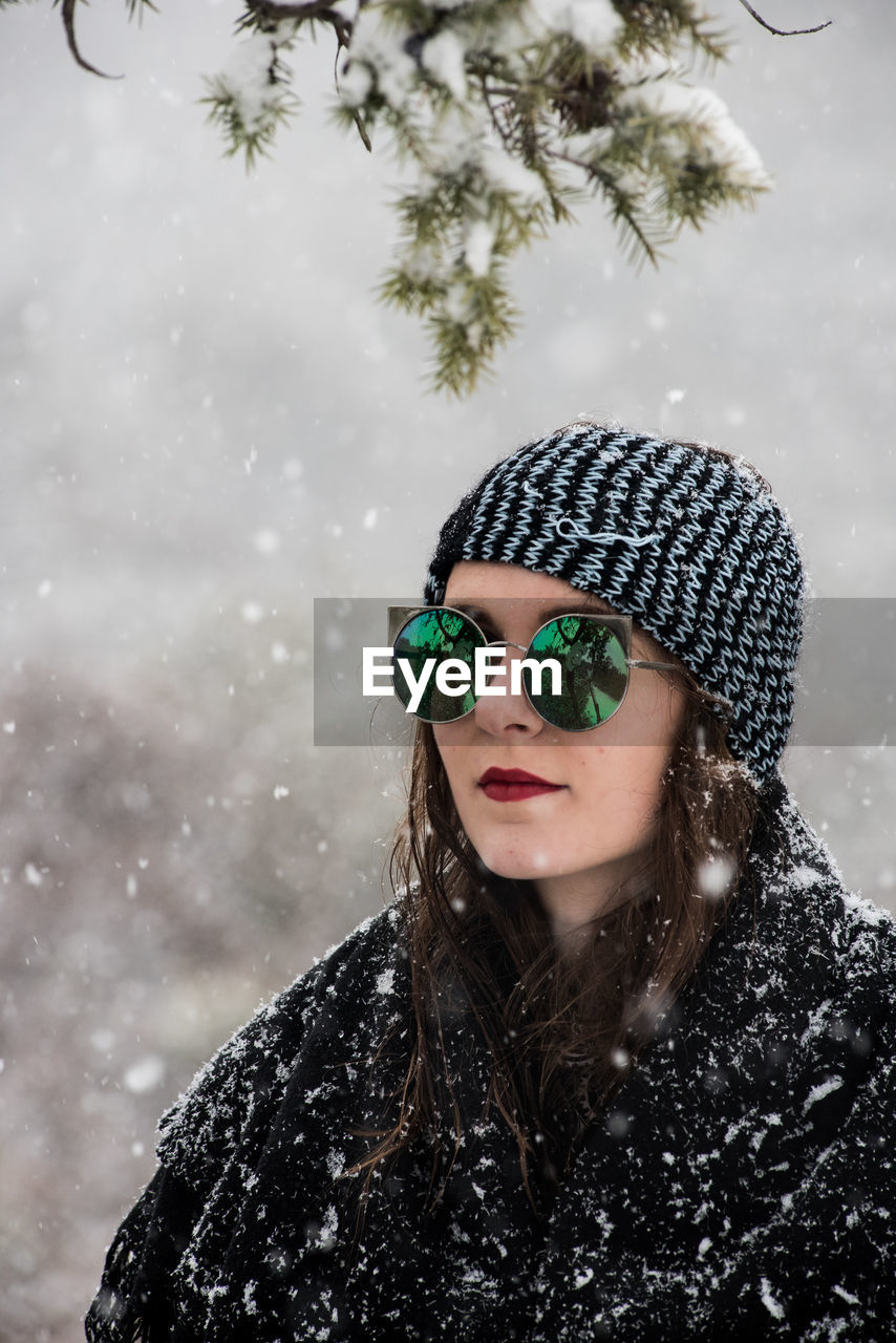 PORTRAIT OF WOMAN WEARING SUNGLASSES AGAINST SNOW