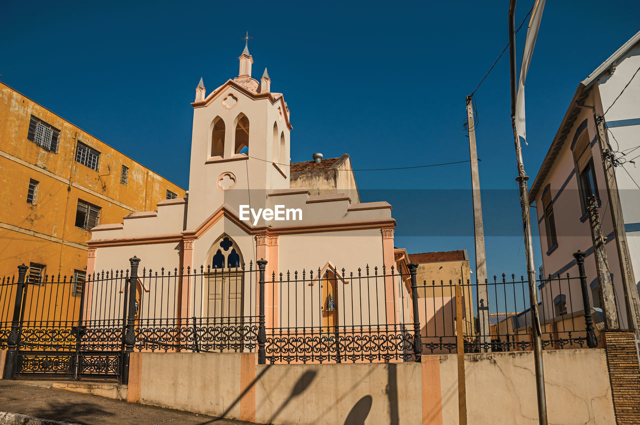 Facade of small church and belfry behind iron fence, in a sunny day at são manuel, brazil.