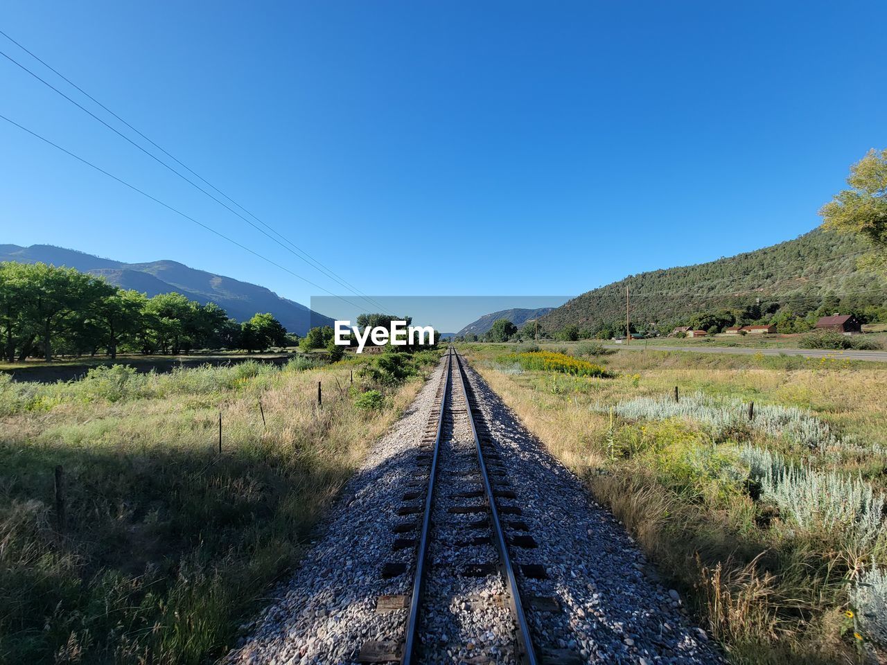 RAILROAD TRACKS ON FIELD AGAINST CLEAR SKY