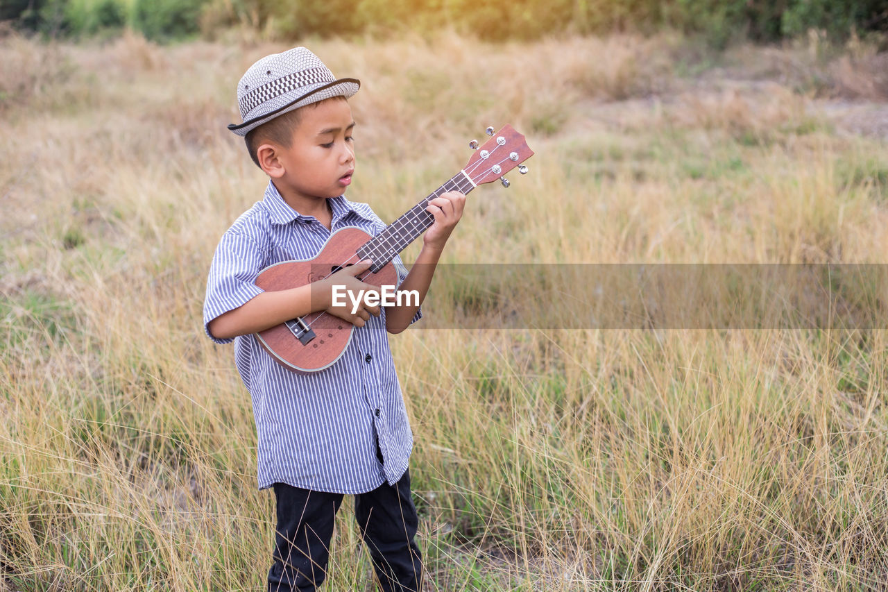 Boy playing ukulele while standing on field