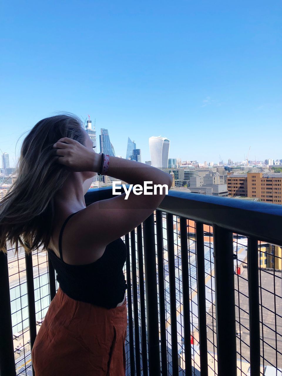 Young woman standing by railing in balcony against sky