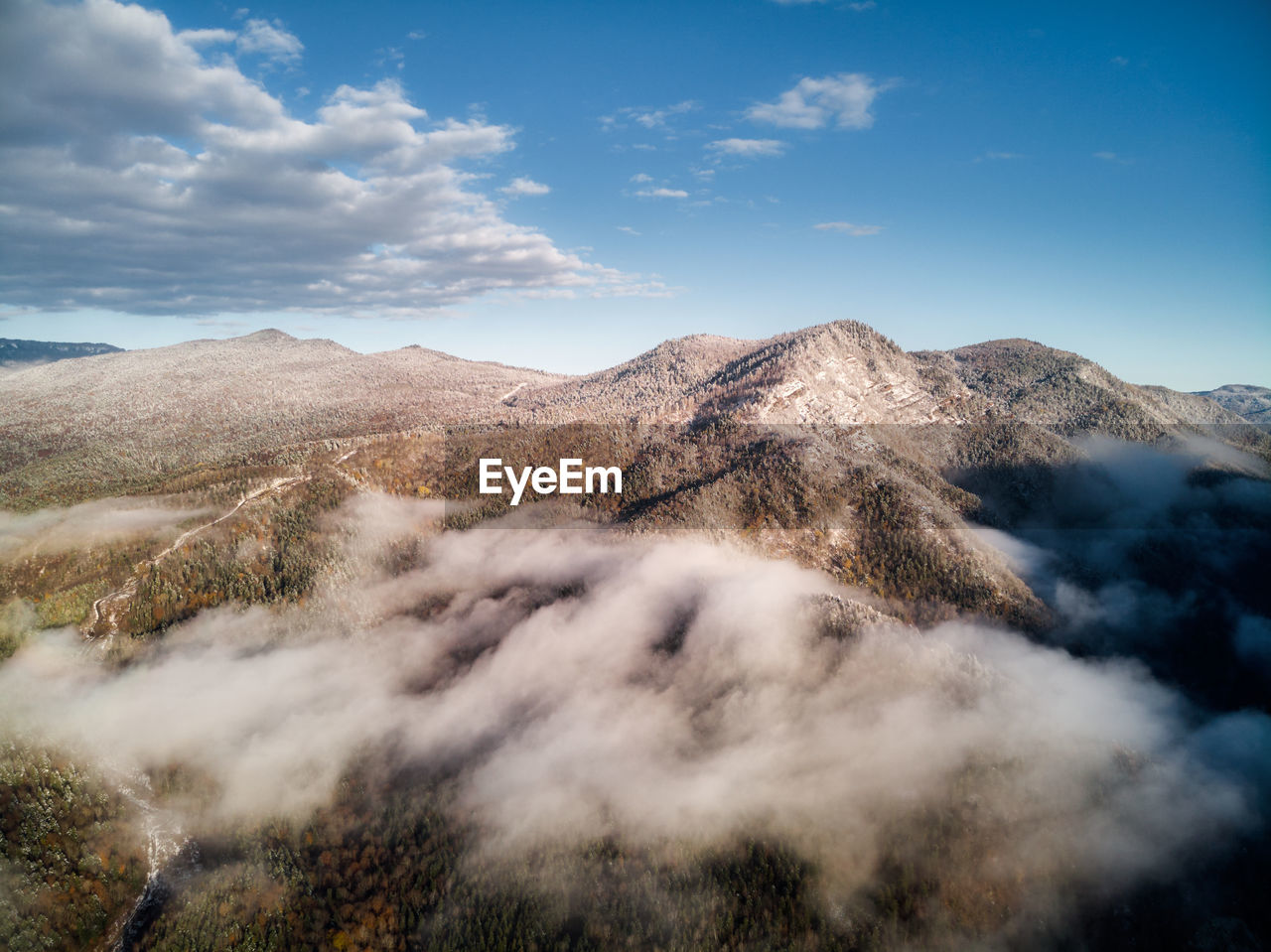 Aerial view, sea of fog and clouds illuminated by the rising sun, snow on the tops of the mountains