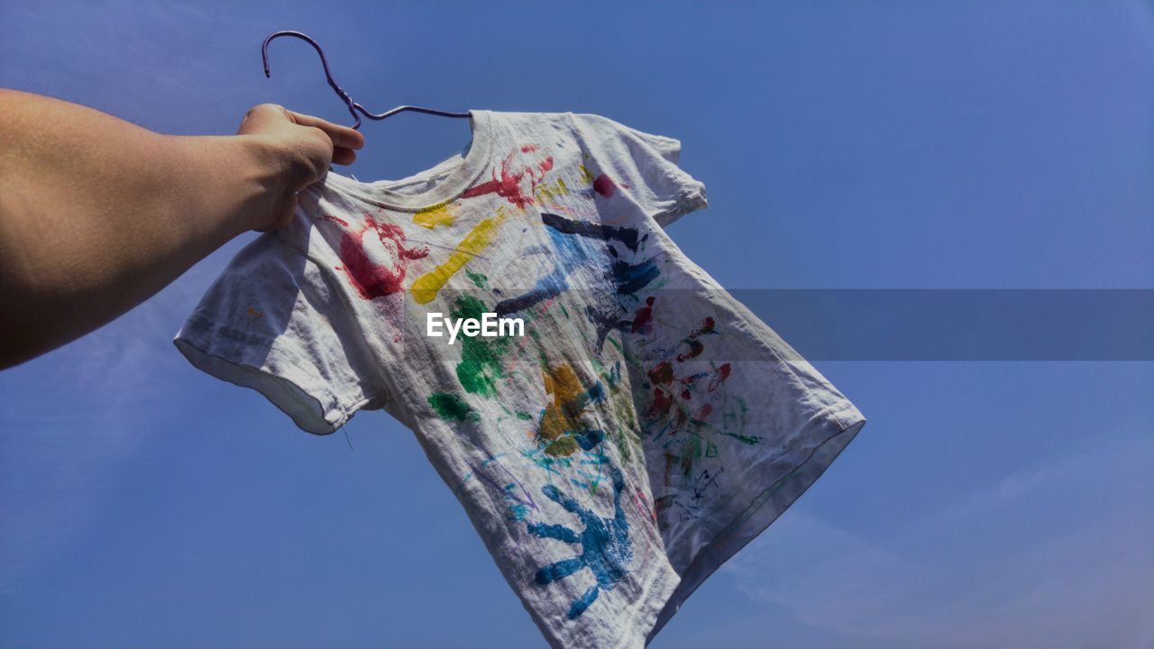 Low angle view of hand holding child's painted t shirt 