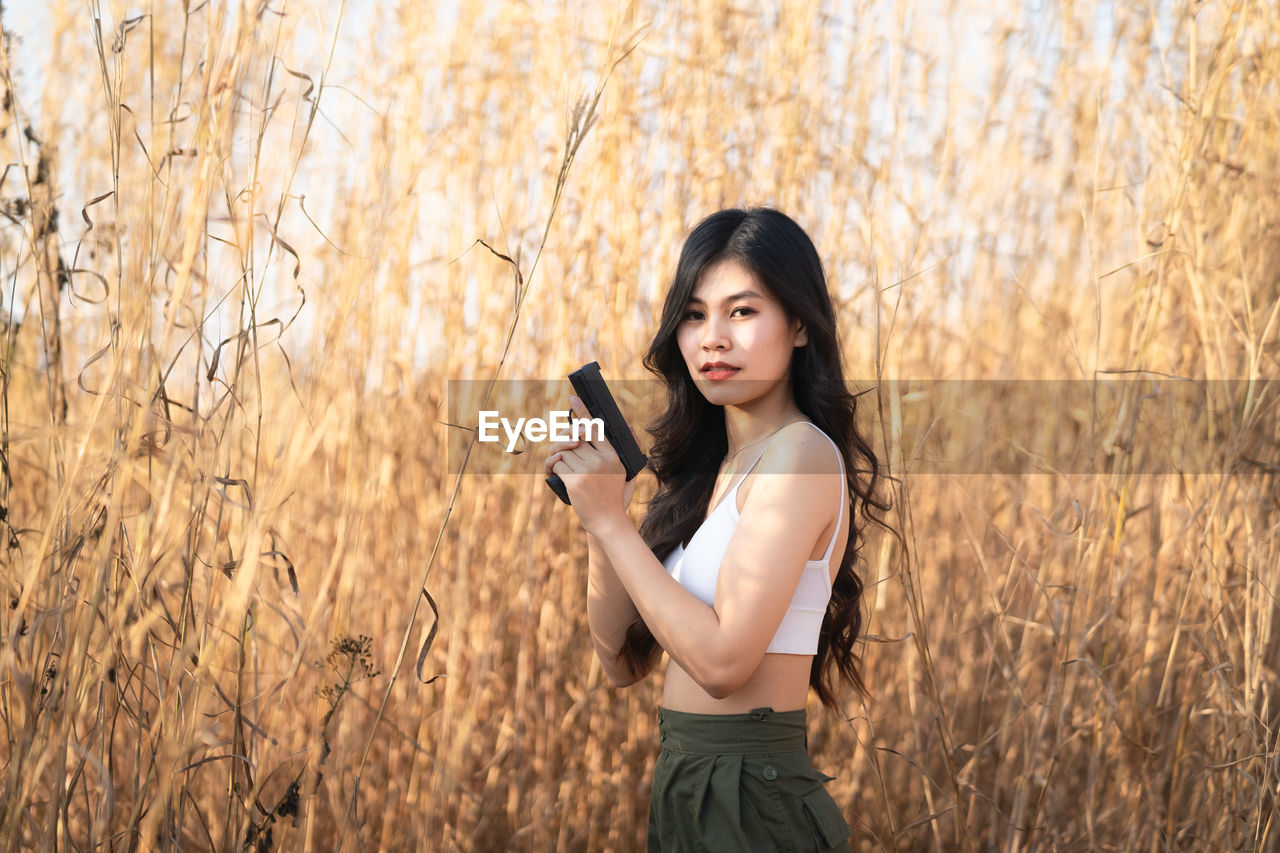 PORTRAIT OF YOUNG WOMAN STANDING IN FIELD