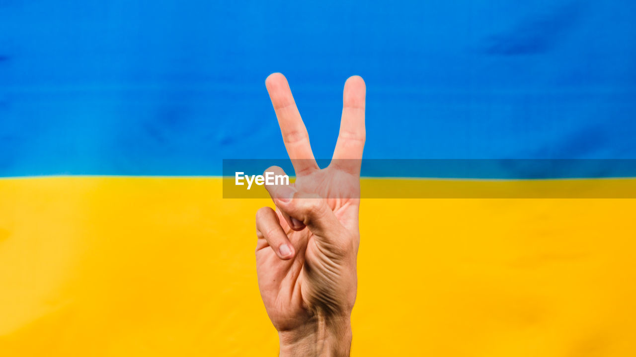 Hand in victory symbol with ukrainian flag for background
