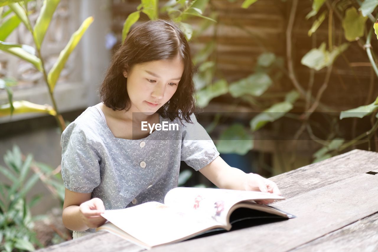 Young woman reading book while sitting at table