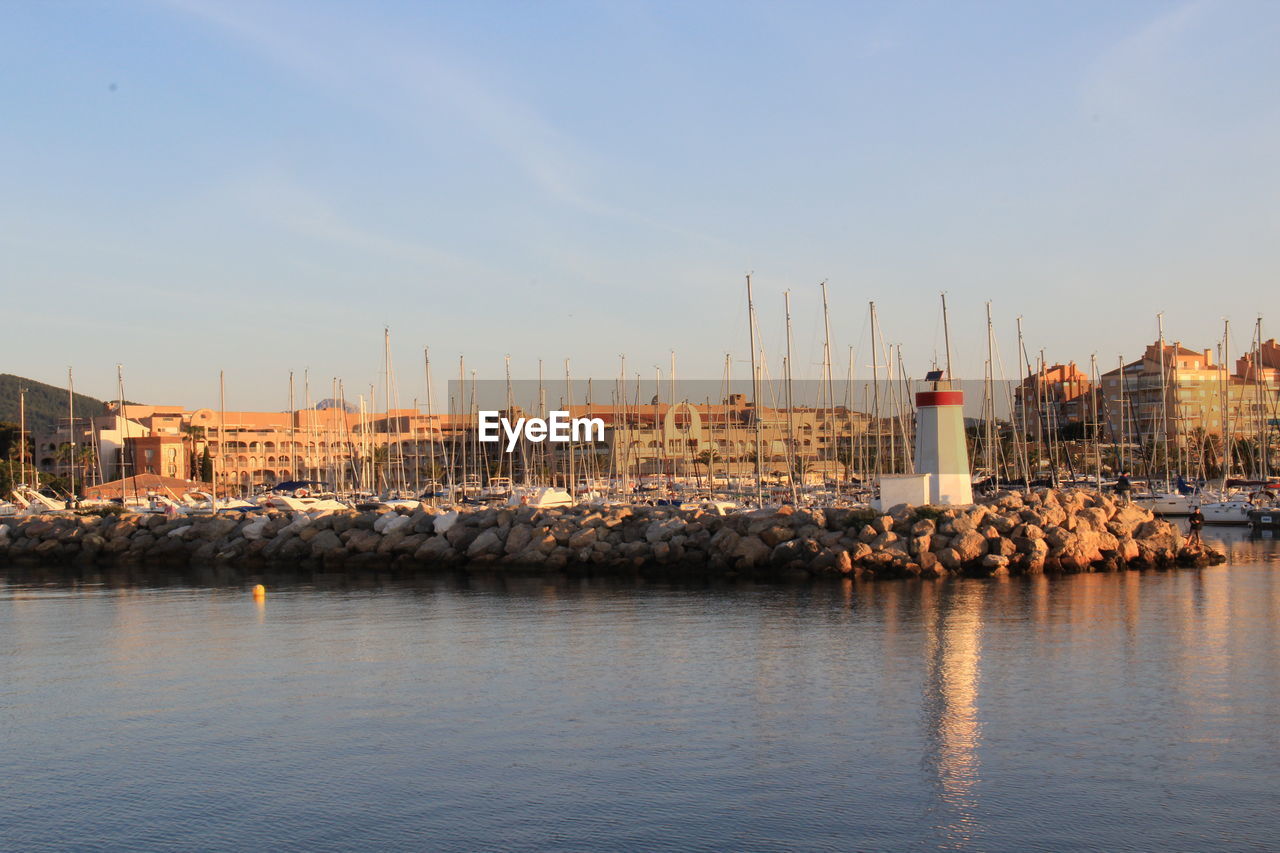 Sailboats in harbor by buildings in city against sky