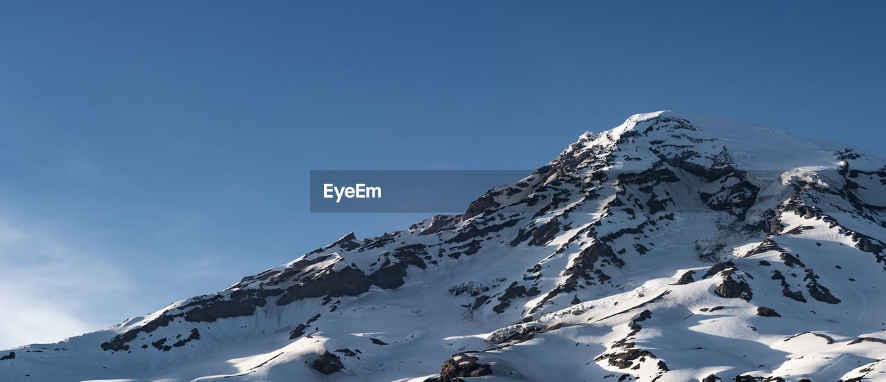 Low angle view of snowcapped mountains against clear blue sky