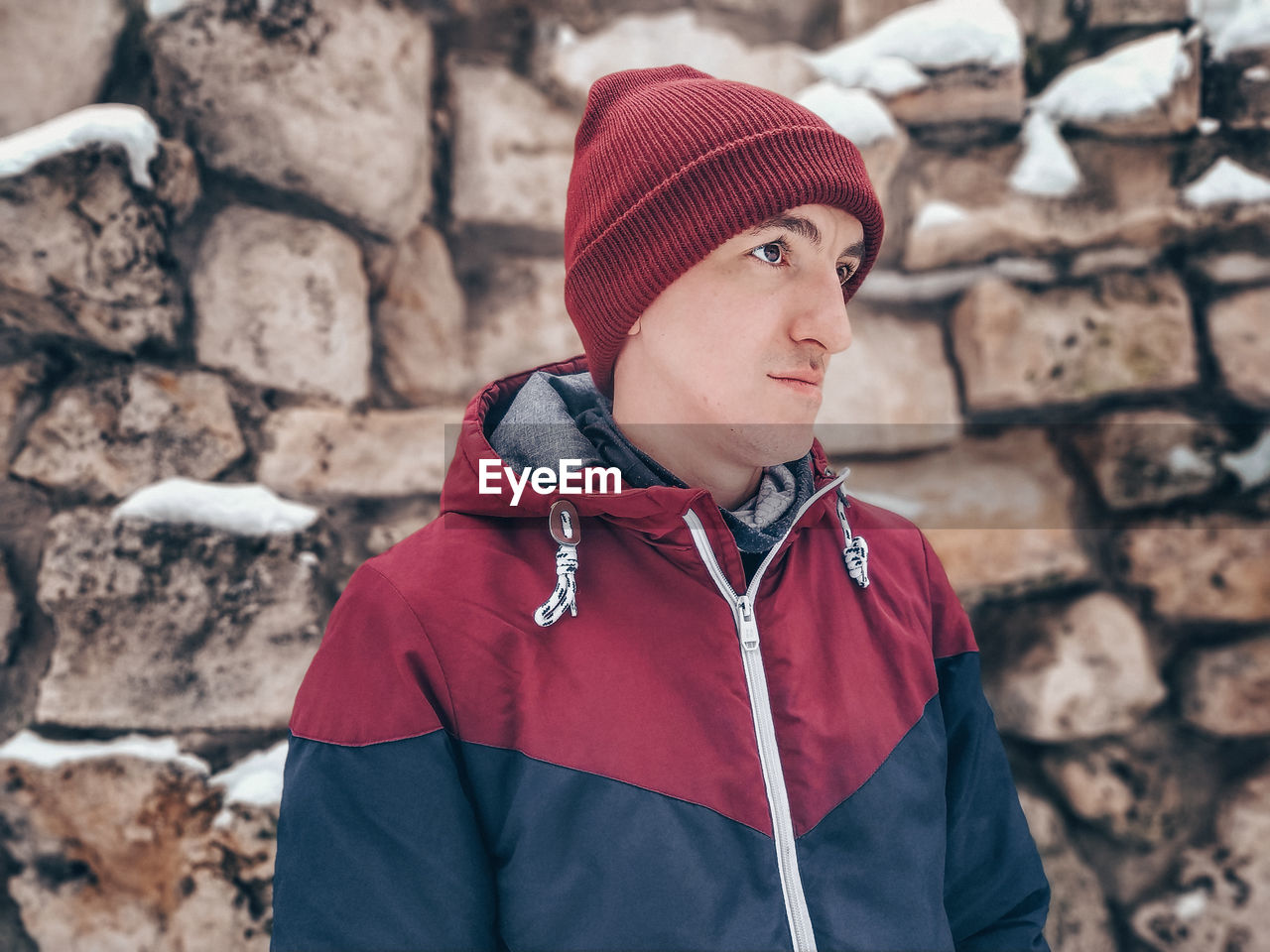 Portrait of man wearing hat standing against stone wall