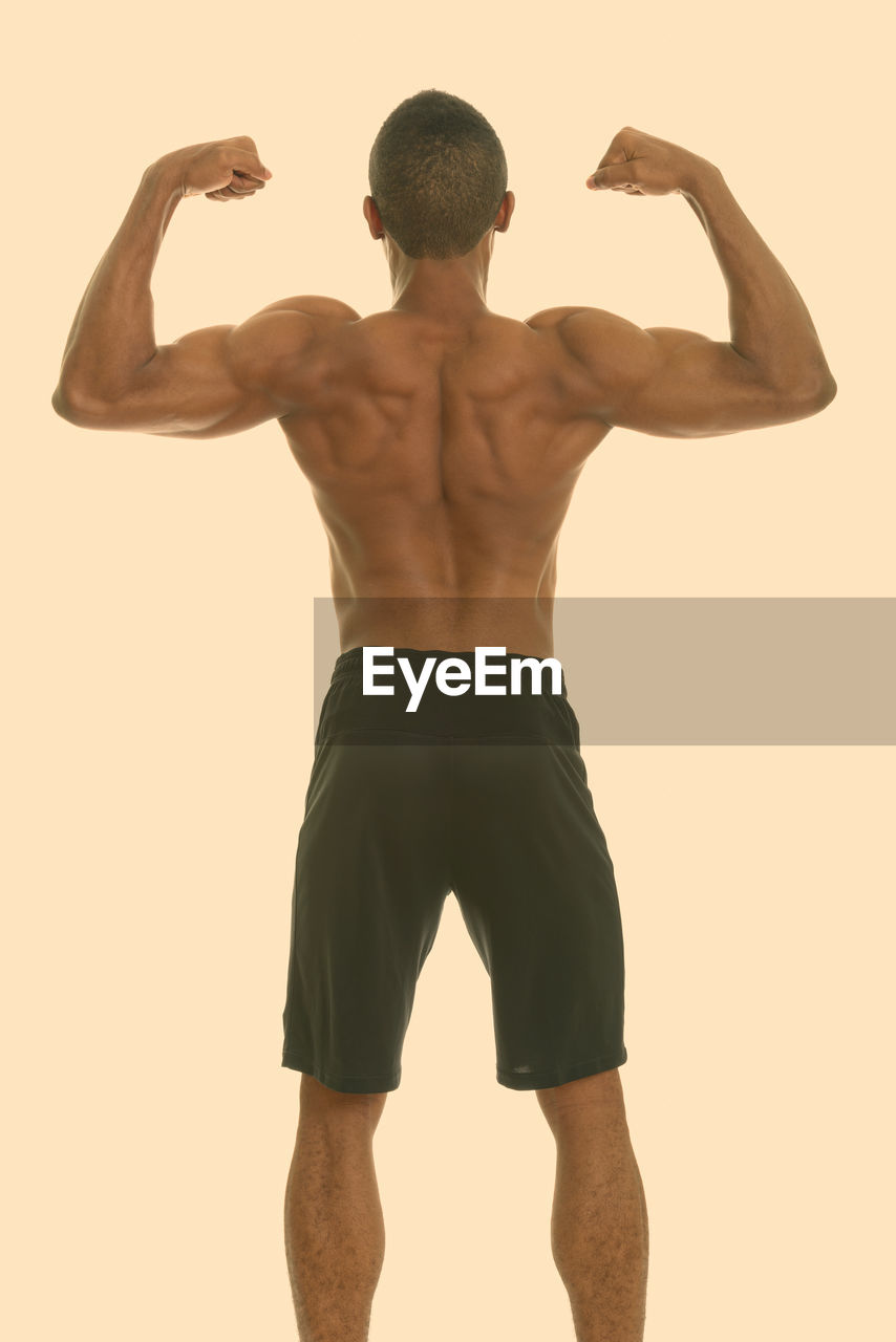 Rear view of shirtless man standing against beige background