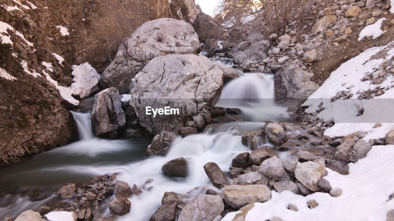 water, winter, scenics - nature, beauty in nature, rock, environment, nature, snow, wilderness, waterfall, landscape, stream, land, cold temperature, motion, river, travel destinations, travel, no people, outdoors, long exposure, rapid, tree, non-urban scene, forest, ice, tourism, flowing water, wadi, tranquility, water feature, flowing, rock formation, mountain, plant