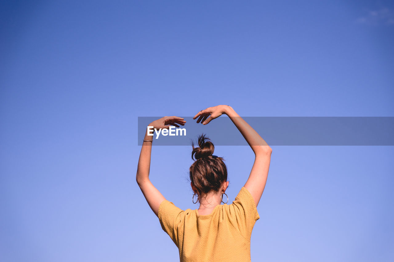 Rear view of woman dancing against clear blue sky