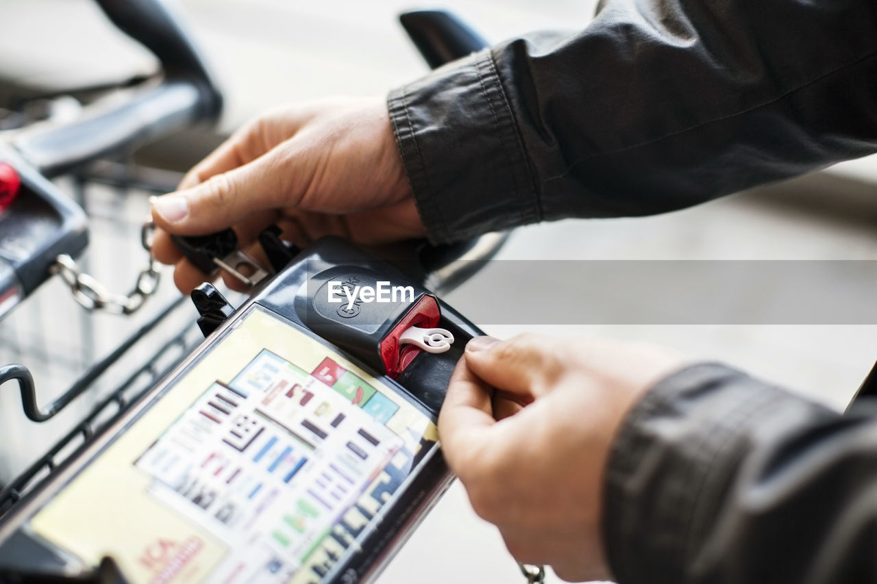 Cropped image of man removing chain from shopping cart in supermarket