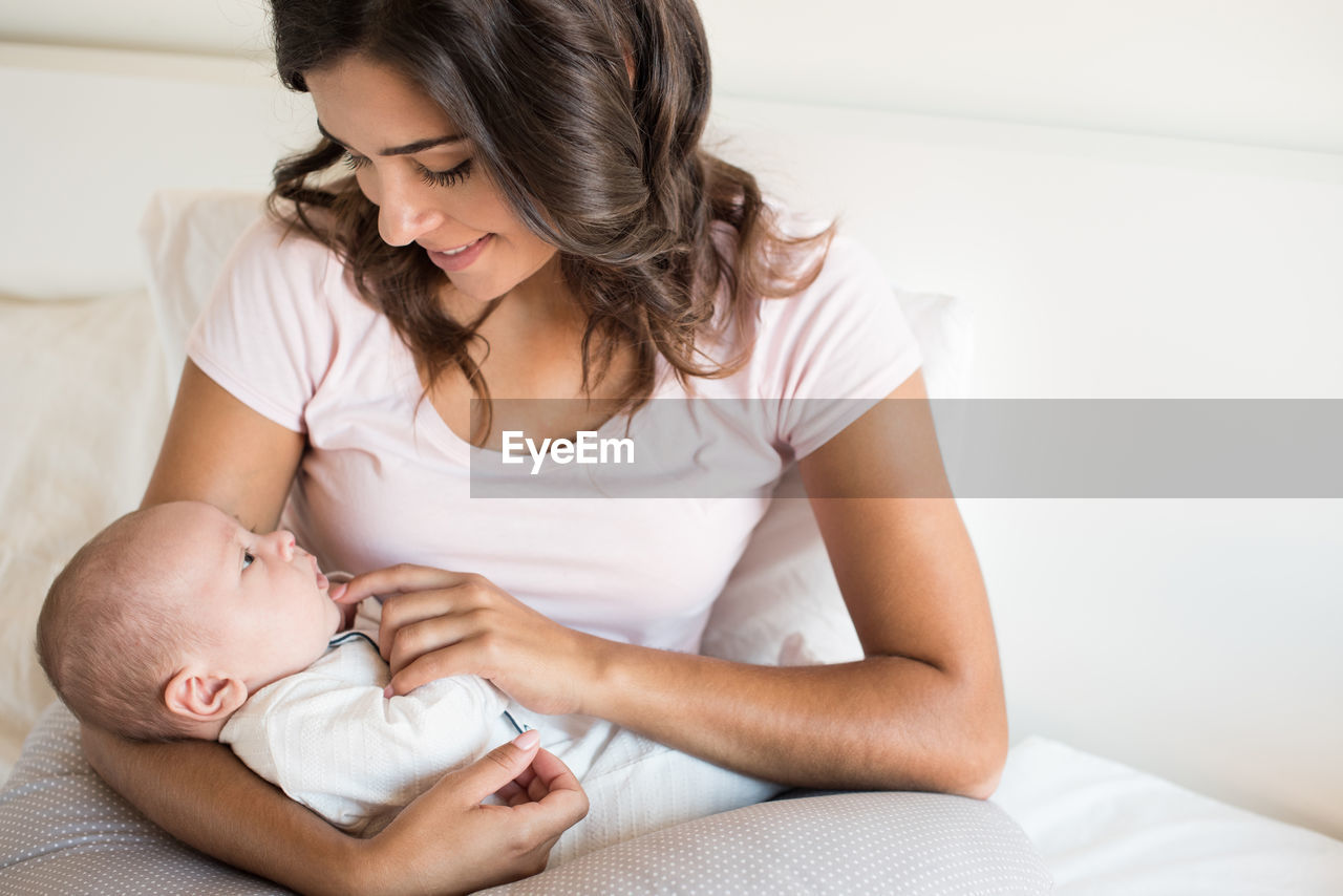 Smiling mother looking at son while sitting on sofa at home