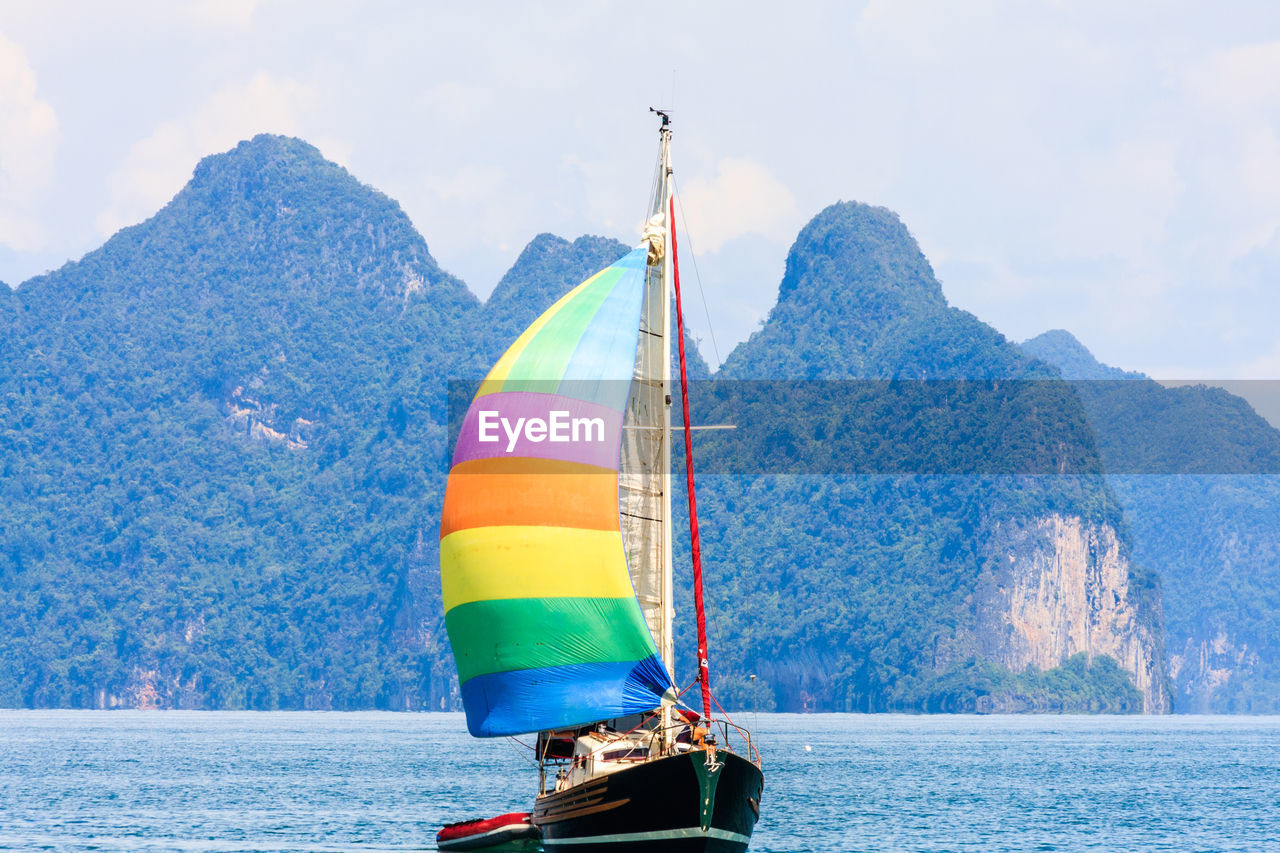 SAILBOAT ON SEA AGAINST MOUNTAIN