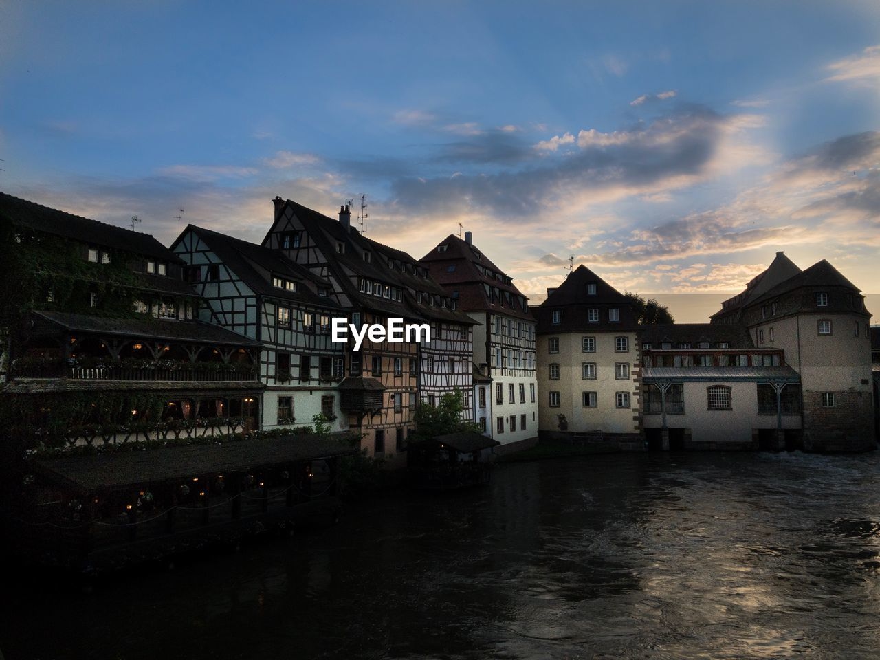 Buildings at waterfront against cloudy sky