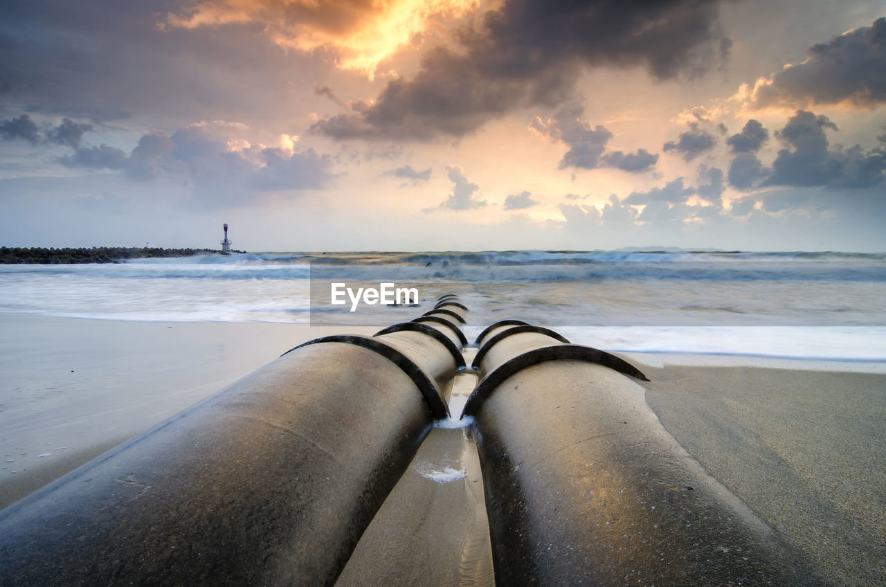 Pipes at beach against sky during sunset