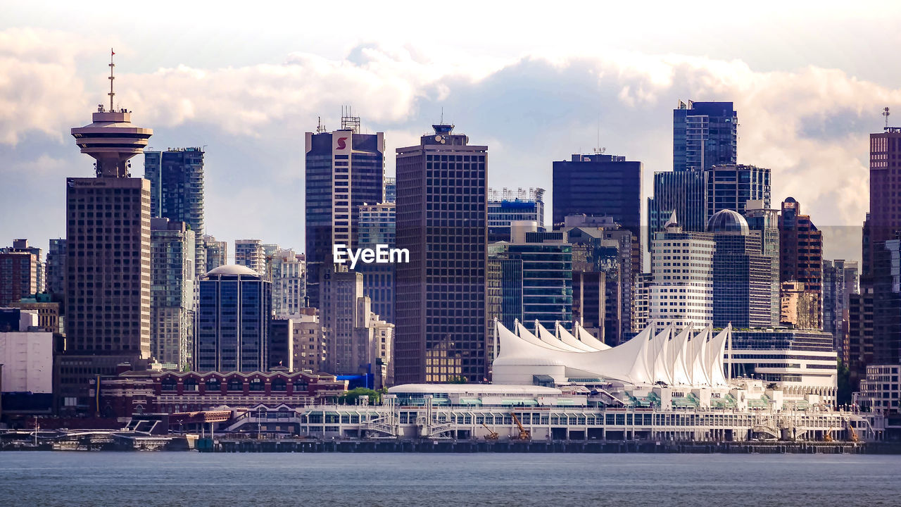 View of buildings in city against cloudy sky with waterfront