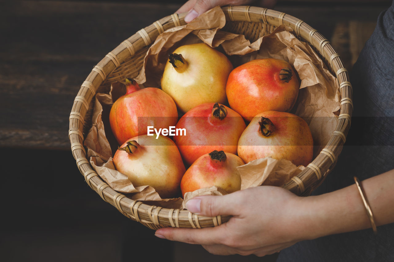 Midsection of woman holding pomegranates in basket